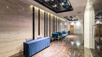 A hotel lobby with a marble wall, a reception desk, blue seating, and a modern ceiling design.