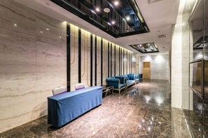 Un vestíbulo de hotel con pared de mármol, mostrador de recepción, asientos azules y un diseño moderno del techo.