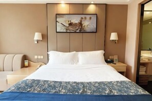 A hotel room with a large bed, two bedside tables, a desk, a chair, and a bathroom visible through an open door. - Xiamen Yinhai Blue Hotel (Gaoqi Airport Wuyuan Bay Branch) (Xiamen)