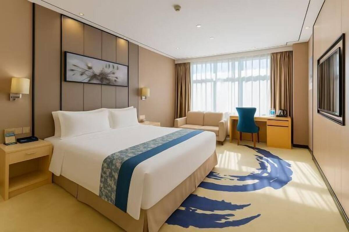 A hotel room with a large bed, a desk, a chair, a TV, and a window with curtains.