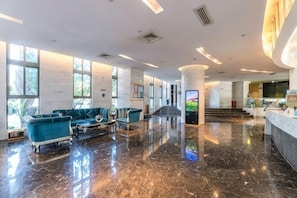 Um hall amplo com piso de mármore, um balcão de recepção e uma área de estar com sofás.