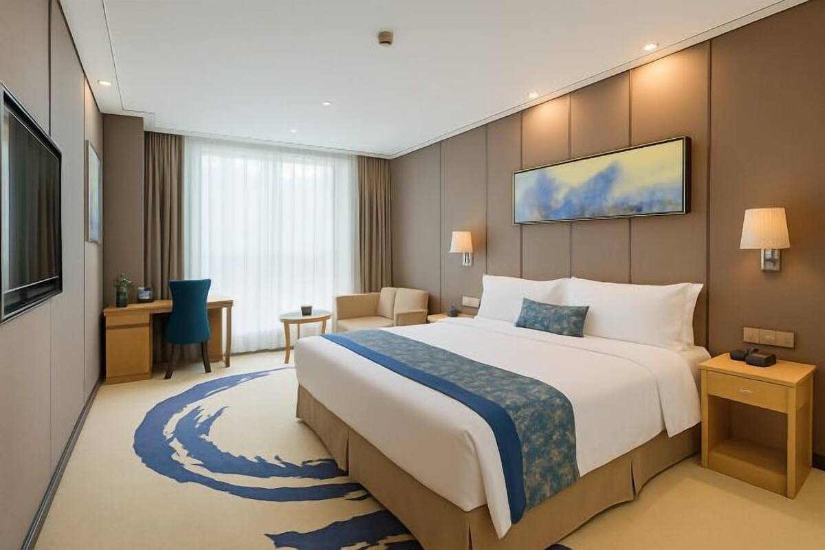 A hotel room with a large bed, a desk, a chair, a small table, and a TV.