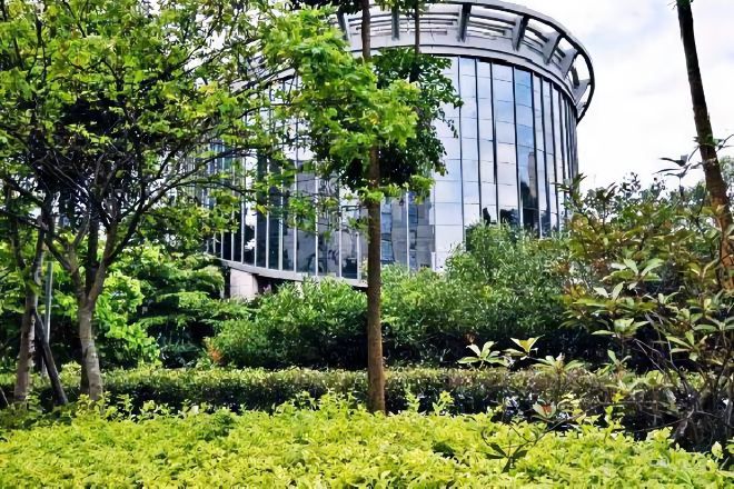 A modern building with a curved glass facade surrounded by lush greenery.