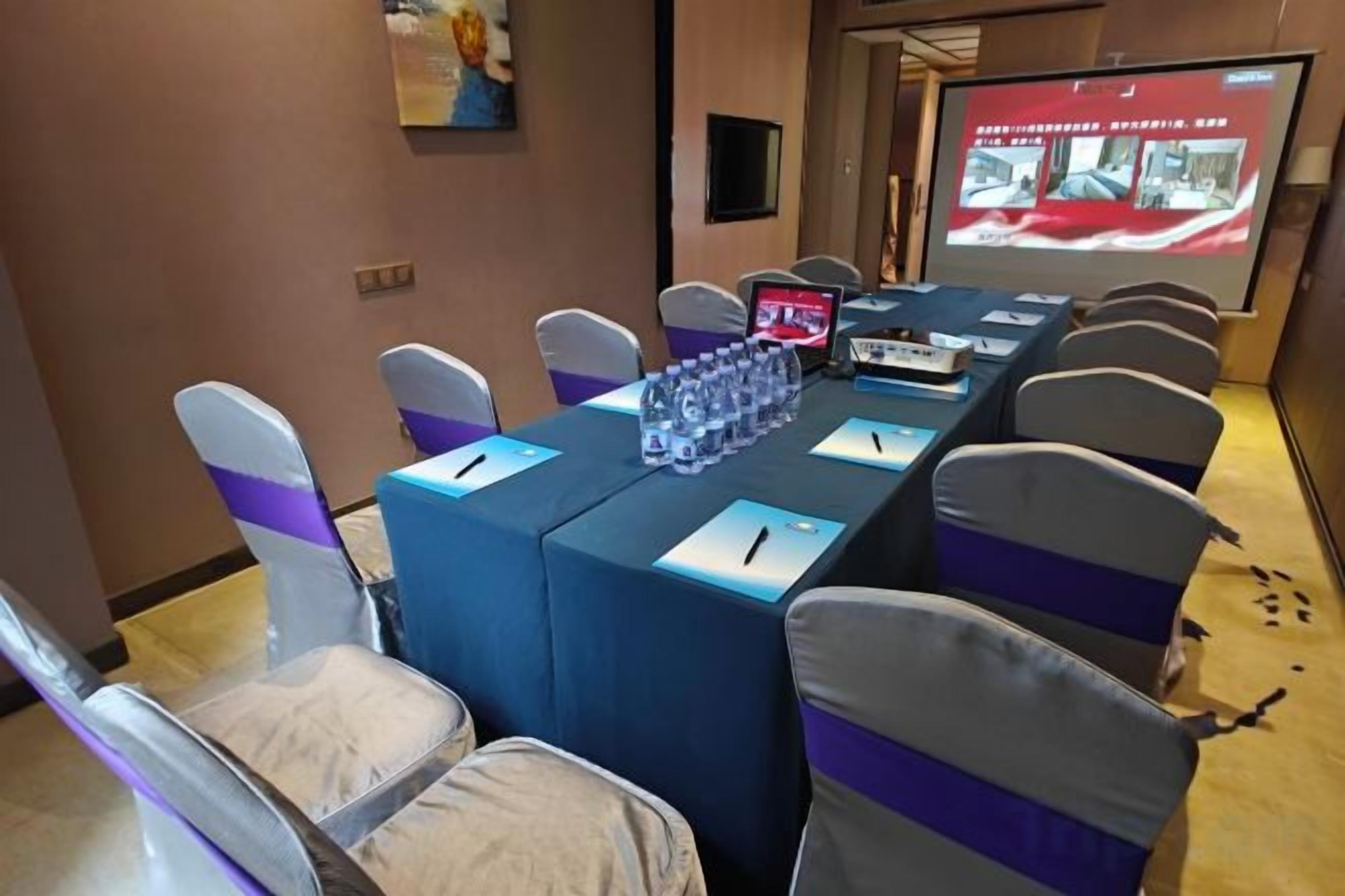 Une salle de conférence équipée d’une longue table, de chaises, d’un écran de projection et d’un ordinateur portable.