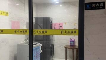 A hotel room with a washing machine, a small table with a purple item, and a sign indicating a laundry area.