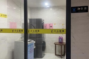 Habitación de hotel con lavadora, una mesita y un objeto morado, además de un letrero que indica una zona de lavandería.