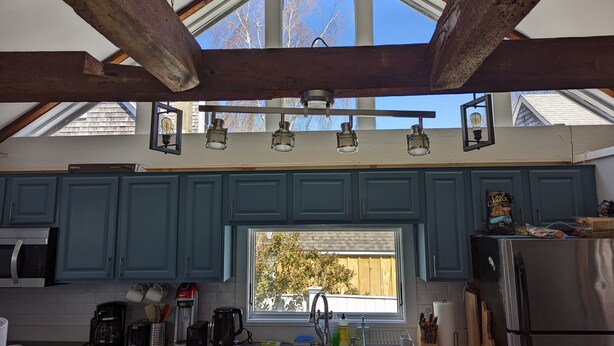 A kitchen with blue cabinets, a stainless steel refrigerator, and a window with a view of trees. - Be right in the action in our centrally-located 2BR/1BA condo with Hot Tub (Provincetown)