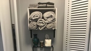Un baño pequeño con inodoro, repisa con toallas, un florero y una caja de pañuelos.