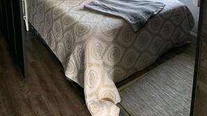 Un dormitorio ordenado con cama, cortinas, un cuadro enmarco y un jarrón con flores.
