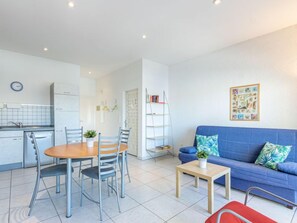Een moderne woonkamer met een blauwe bank, een houten salontafel en een eethoek met een ronde tafel en stoelen.