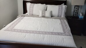 A neatly made bed with a wooden headboard, a bedside table with a lamp, and a wall-mounted nightstand. - Jane's Hideaway (Frederiksted)