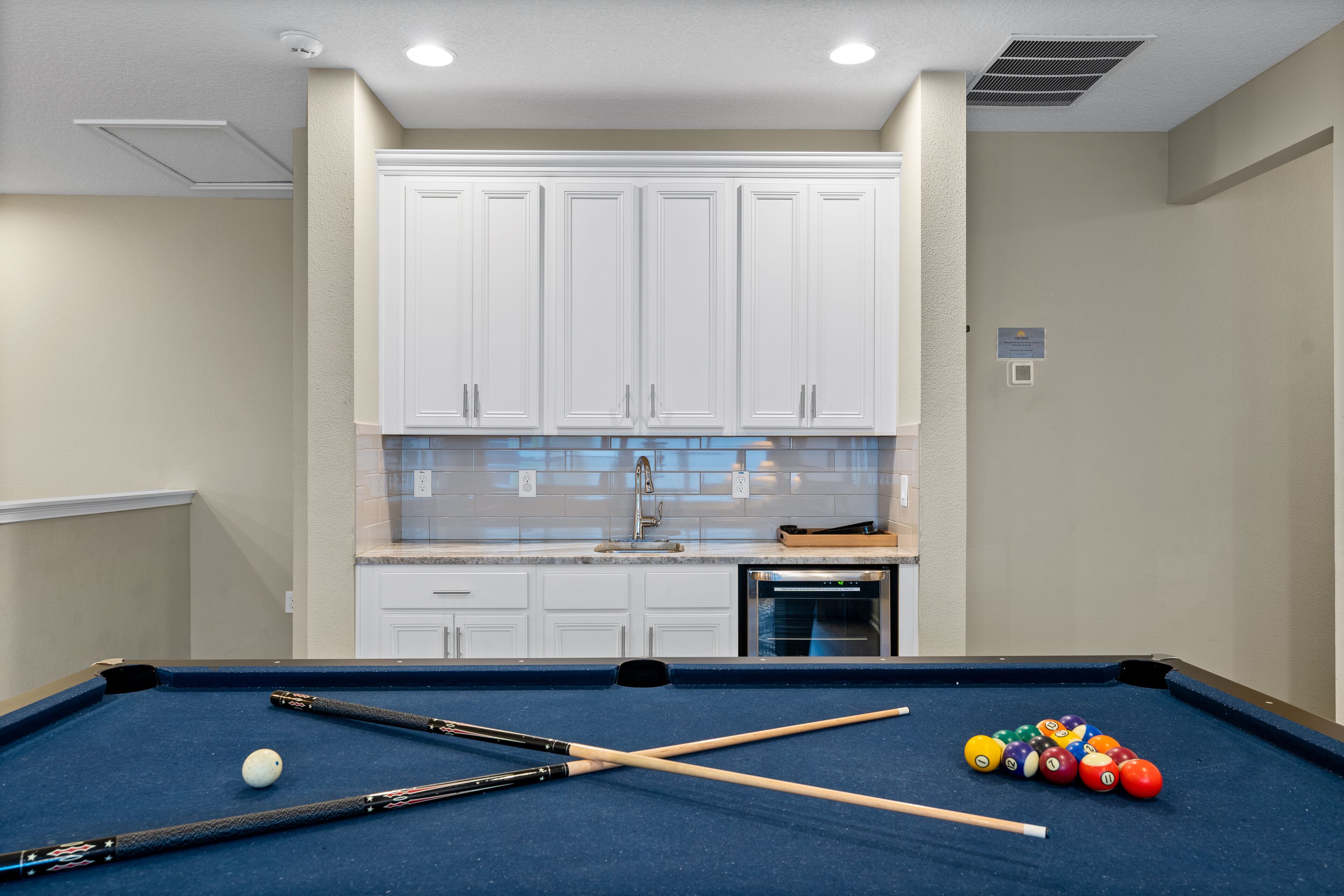 A pool table with pool cues and balls, a kitchen area with white cabinets, and a built-in oven.