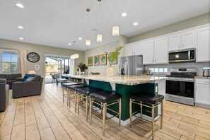 A modern kitchen with white cabinets, stainless steel appliances, and a green island with bar stools. - Theater / Games Areas | Kids Bedrooms | Screened Pool | Kids Bedrooms | Screened Pool (Davenport)