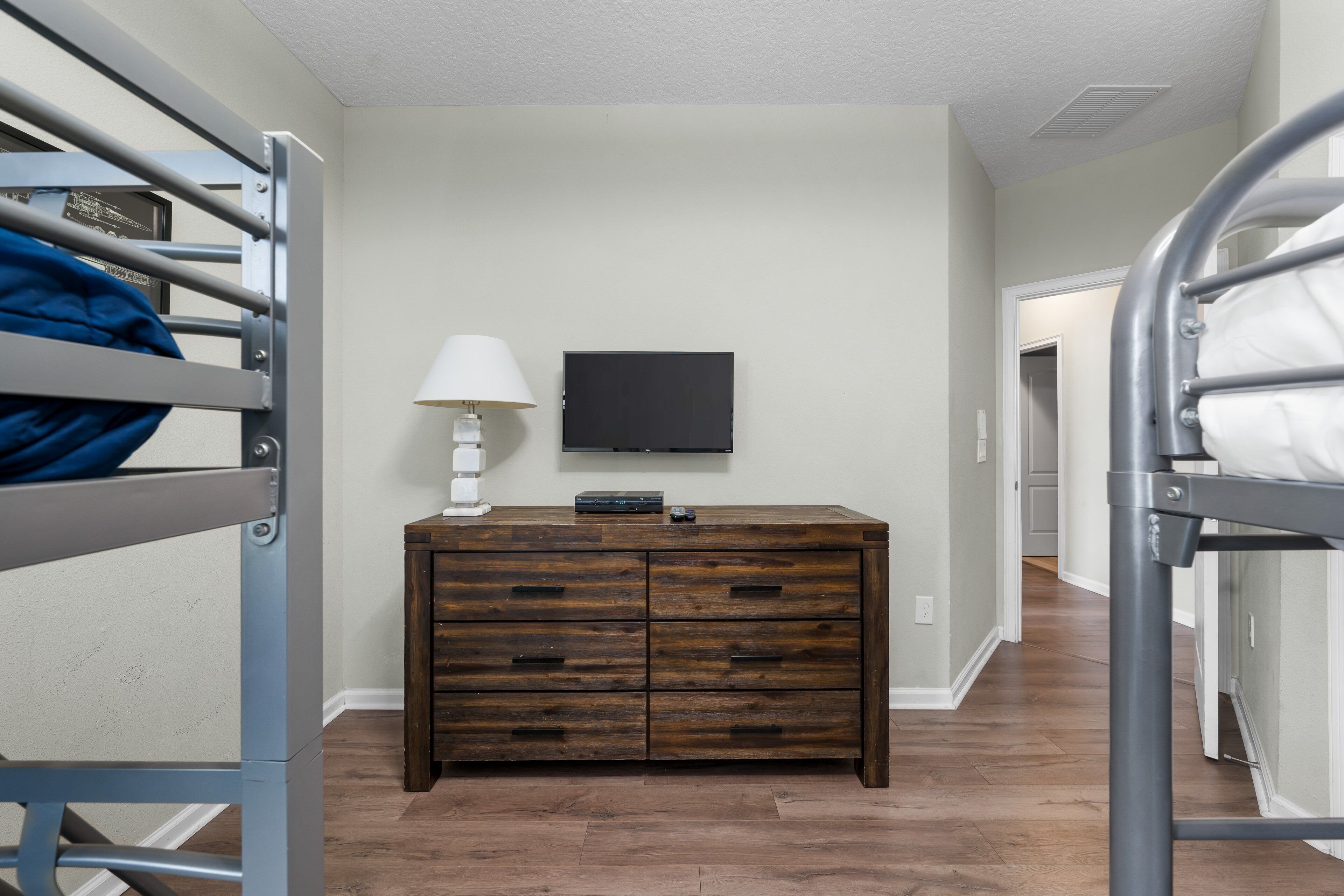 A bunk bed room with a wooden dresser, a lamp, and a flat-screen TV on the wall.