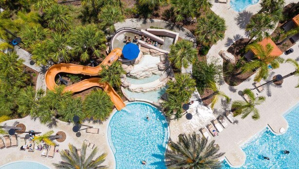 Luchtbeeld van een resort met een groot zwembad, een glijbaan en palmbomen.