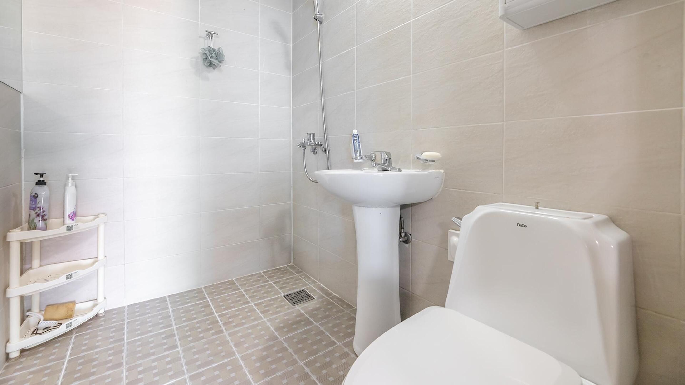 A bathroom with a toilet, sink, and shower. There are toiletries on a shelf.