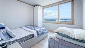 Une chambre avec deux lits, une grande fenêtre donnant sur la mer et un ventilateur de plafond.