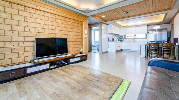 Un salon moderne avec un téléviseur, un mur en bois et une cuisine en arrière-plan.