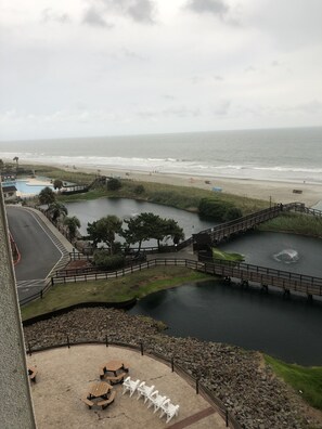 Vista de una playa, un lago pequeño y un puente que los conecta. Hay mesas y sillas de picnic cerca del lago.