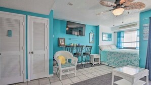 A room with teal walls, a bed with a floral bedspread, a white wicker chair, a small white table, and a ceiling fan. - Beautiful view At Myrtle Beach Resort (Myrtle Beach)