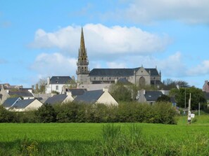A historic building with a prominent spire, surrounded by residential houses and a green field.