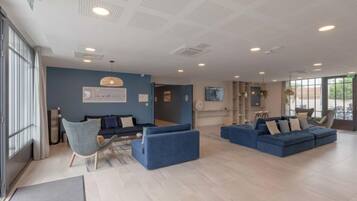 Un salon moderne avec des canapés bleus, une table basse et une cheminée. Une grande fenêtre laisse entrer la lumière naturelle et offre une vue sur l’extérieur.