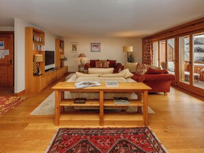 Uma sala de estar acolhedora com uma mesa de centro de madeira, um sofá vermelho, uma televisão e uma estante de livros.