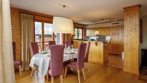 Zona pranzo con tavolo apparecchiato per quattro, pavimento in legno e cucina con mobili impiallacciati.