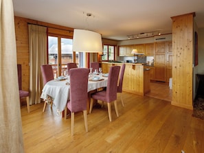 Uma sala de jantar com mesa posta para quatro, piso de madeira e uma cozinha com armários de madeira.