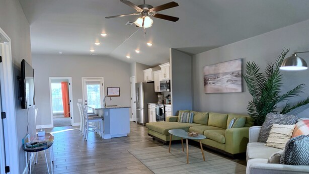 A modern living room with a green sofa, a small coffee table, and a dining area with a white island and chairs. - MODERN HOME - firepit & fenced in backyard! (Carl Junction)