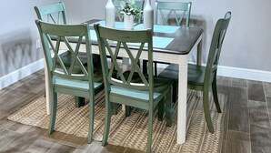 A dining area with a wooden table, green chairs, a large wall clock, and a hanging light fixture. - MODERN HOME - firepit & fenced in backyard! (Carl Junction)