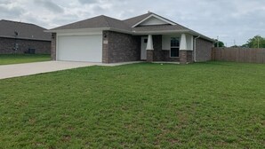 A two-story house with a garage, a covered porch, and a fenced backyard. - MODERN HOME - firepit & fenced in backyard! (Carl Junction)