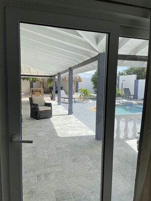 A covered outdoor area with a pool, lounge chairs, and a seating area with a table and chairs.