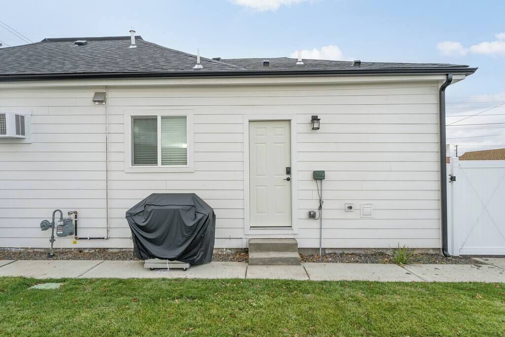 A single-story house with a white exterior, a front door, and a covered grill.
