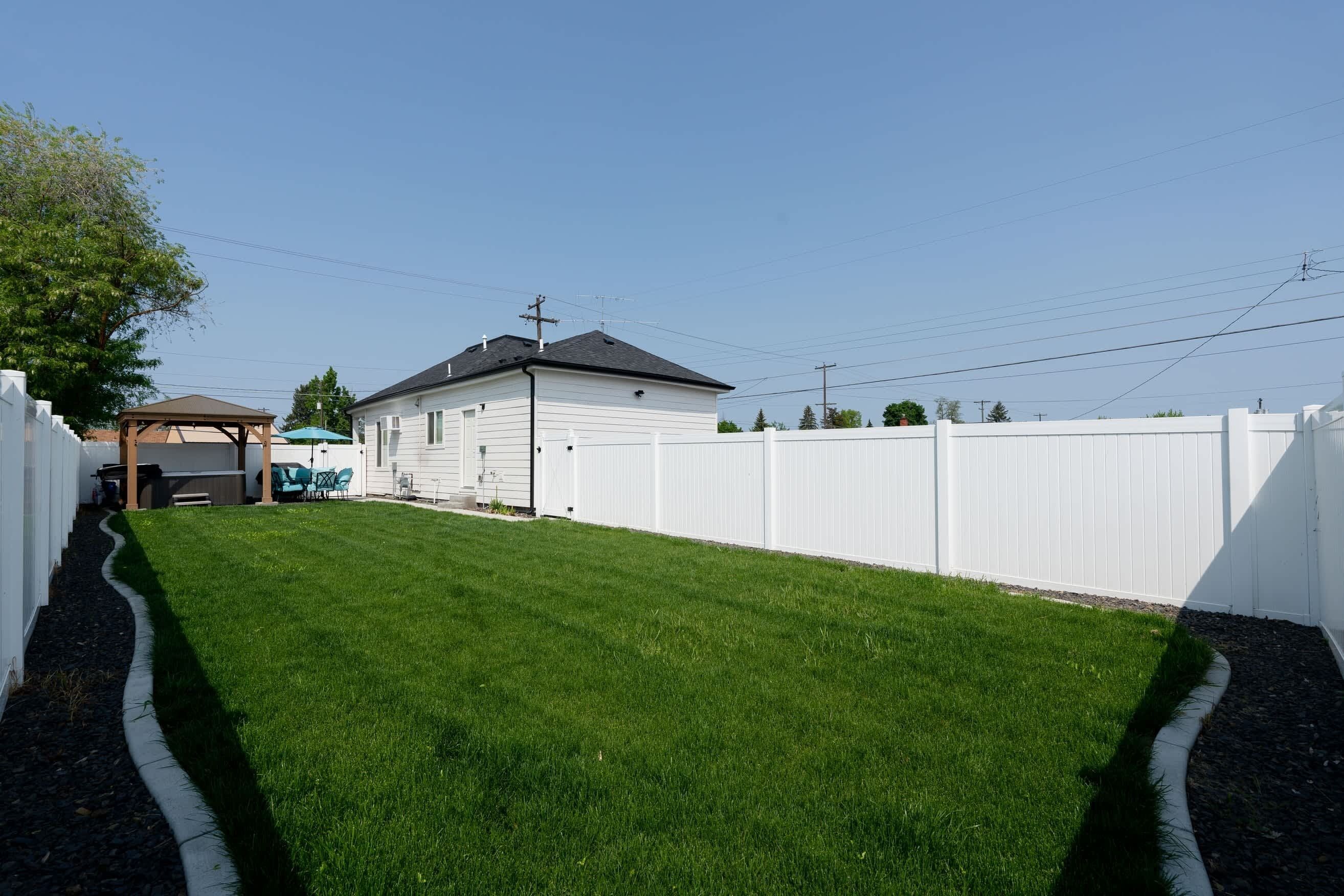 A backyard with a white fence, a lawn, a shed, and a house.