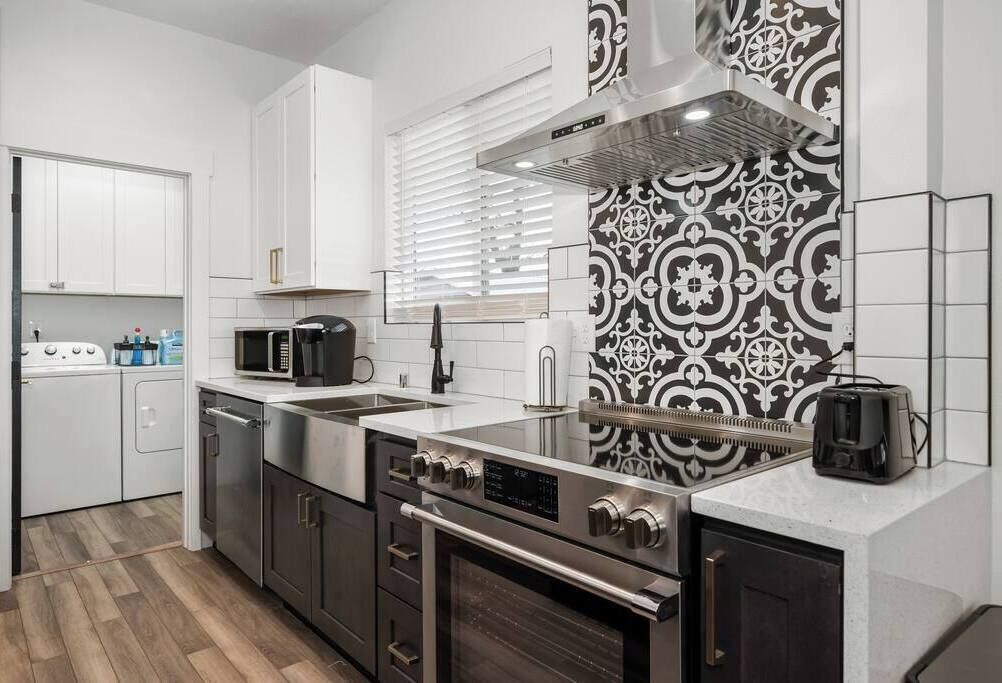 A modern kitchen with stainless steel appliances, white cabinets, and a patterned backsplash.
