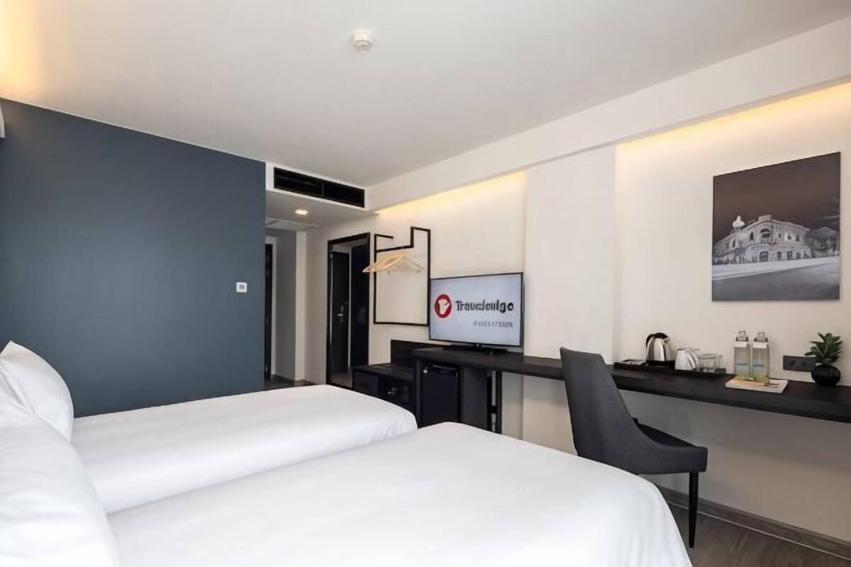 A hotel room with a bed, a desk with a computer, a television, and a framed picture on the wall.