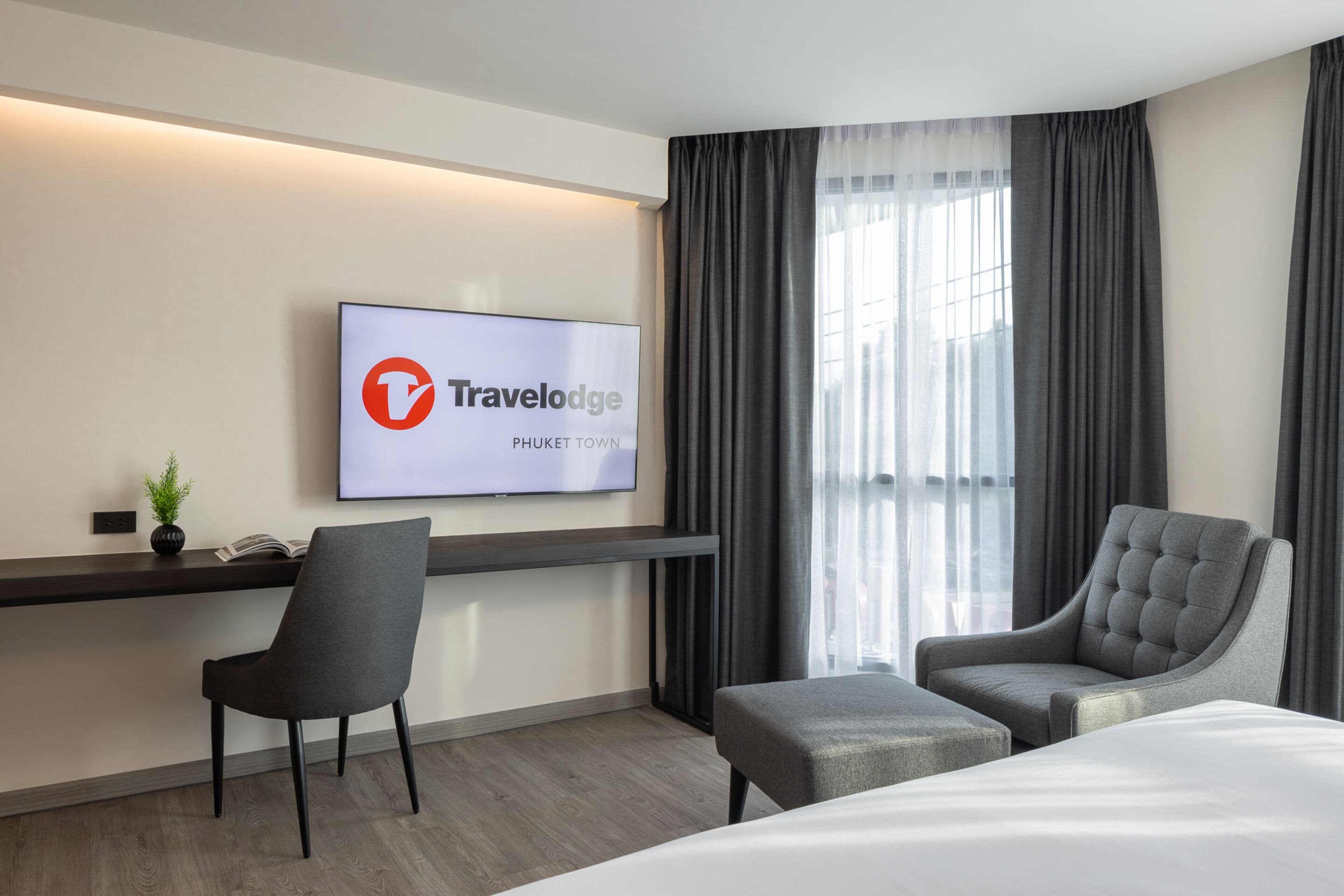 Una camera d'albergo moderna con un letto, una scrivania, una sedia e una TV che mostra il logo Travelodge.