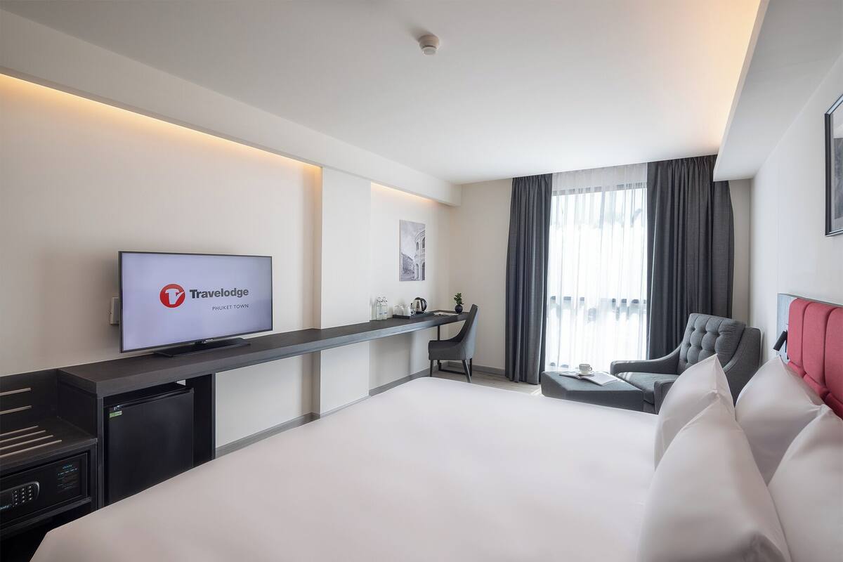 A modern hotel room with a large bed, a desk, a television, and a view of the city.