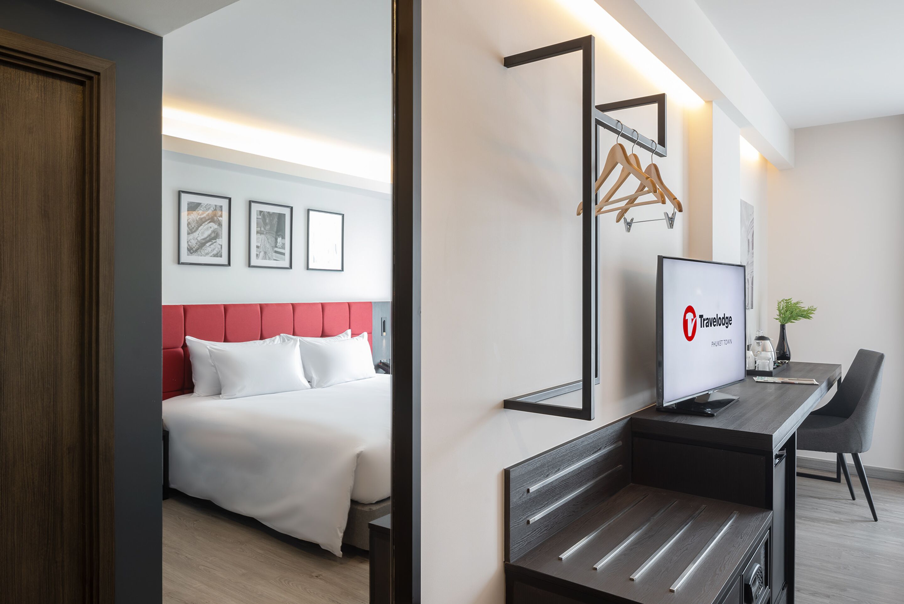 Una habitación de hotel con una cama, un escritorio con un ordenador y un televisor mostrando el logotipo de Travelodge.