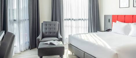 Habitación de hotel con cama, escritorio, silla y televisor mostrando el logotipo de Travelodge.