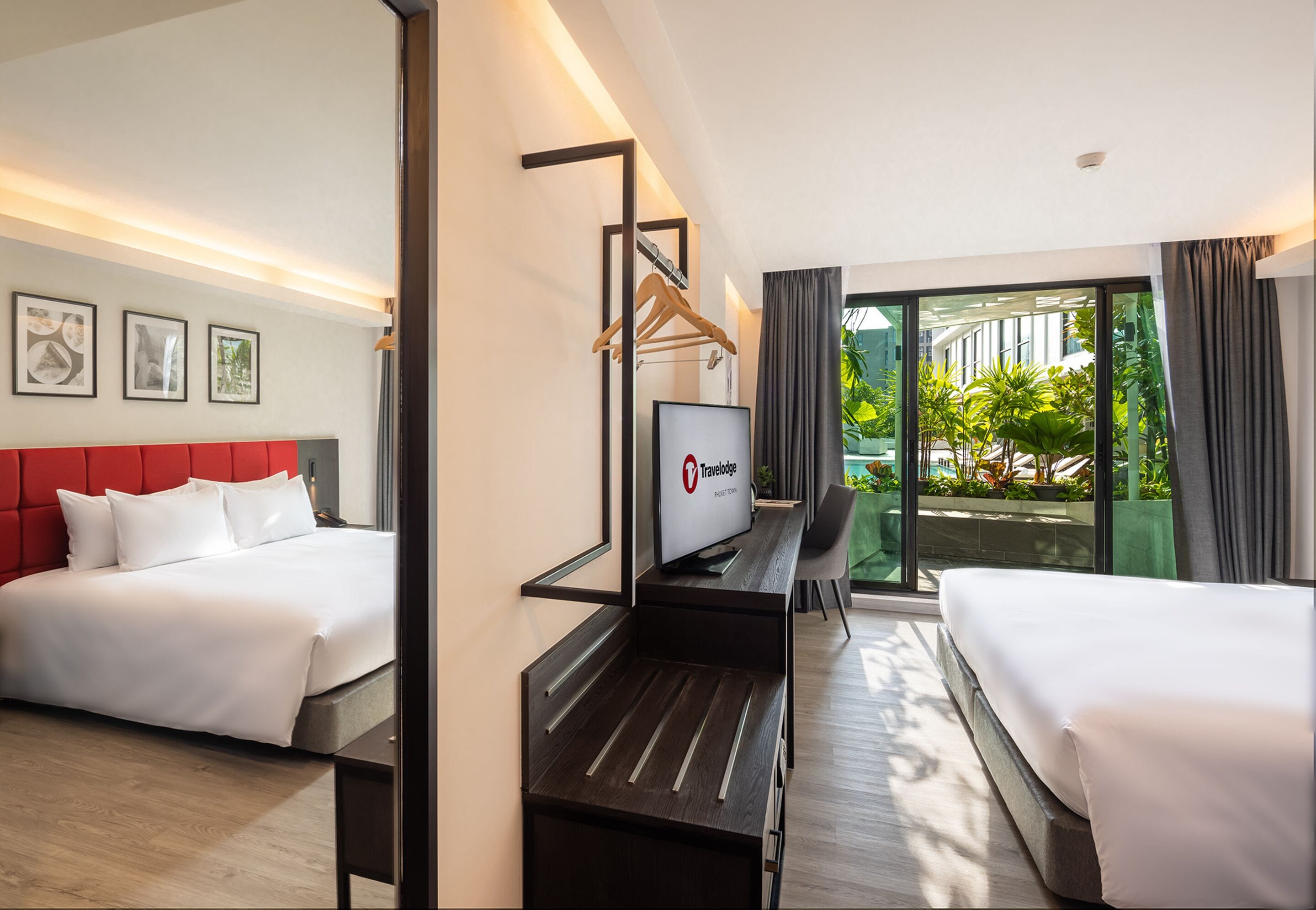 A hotel room with a bed, a desk, a TV, and a view of greenery outside.