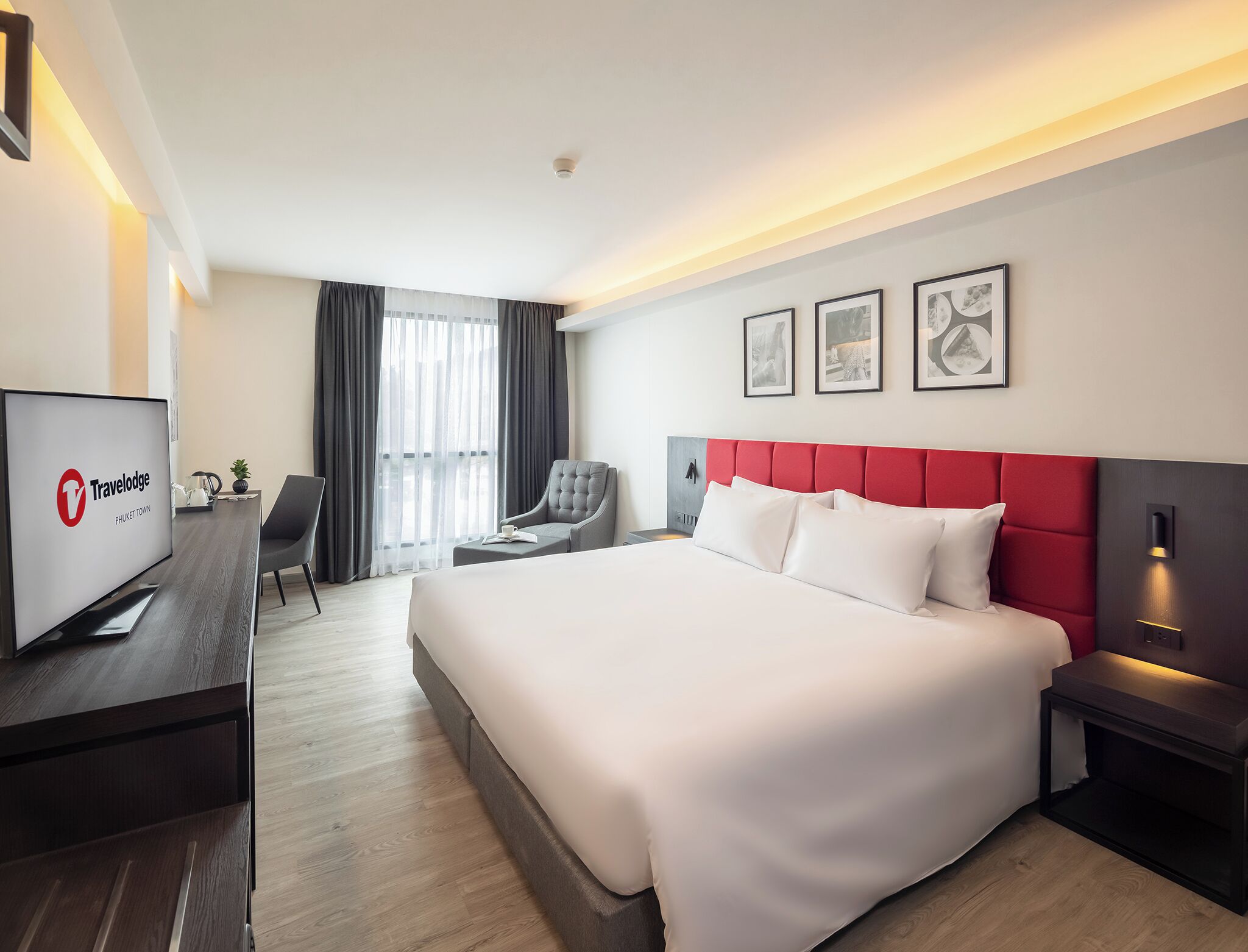 Een hotelkamer met een groot bed, een bureau met een televisie, een stoel en een raam met gordijnen.
