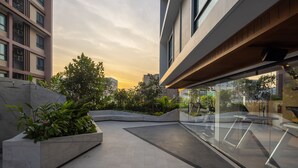 Área externa moderna com piso de azulejos, vasos com vegetação e guarda-corpo de vidro.