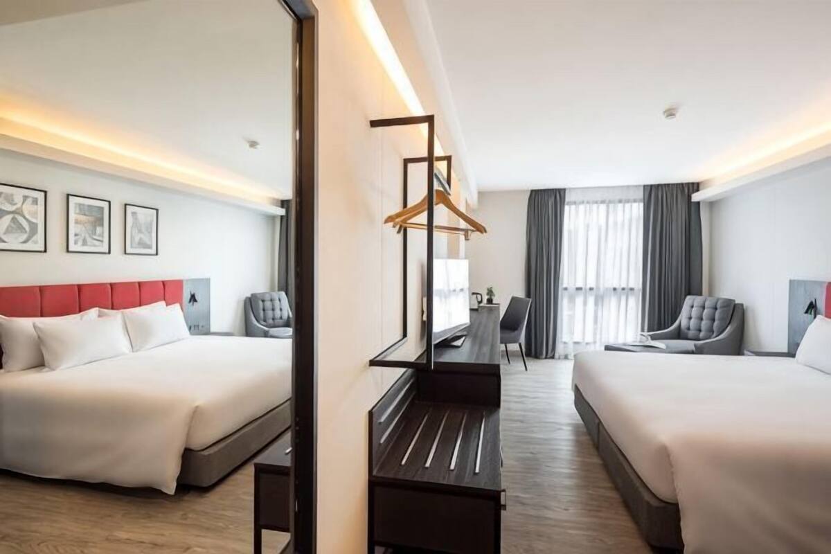 A hotel room with two beds, a desk, a chair, and a mirror.
