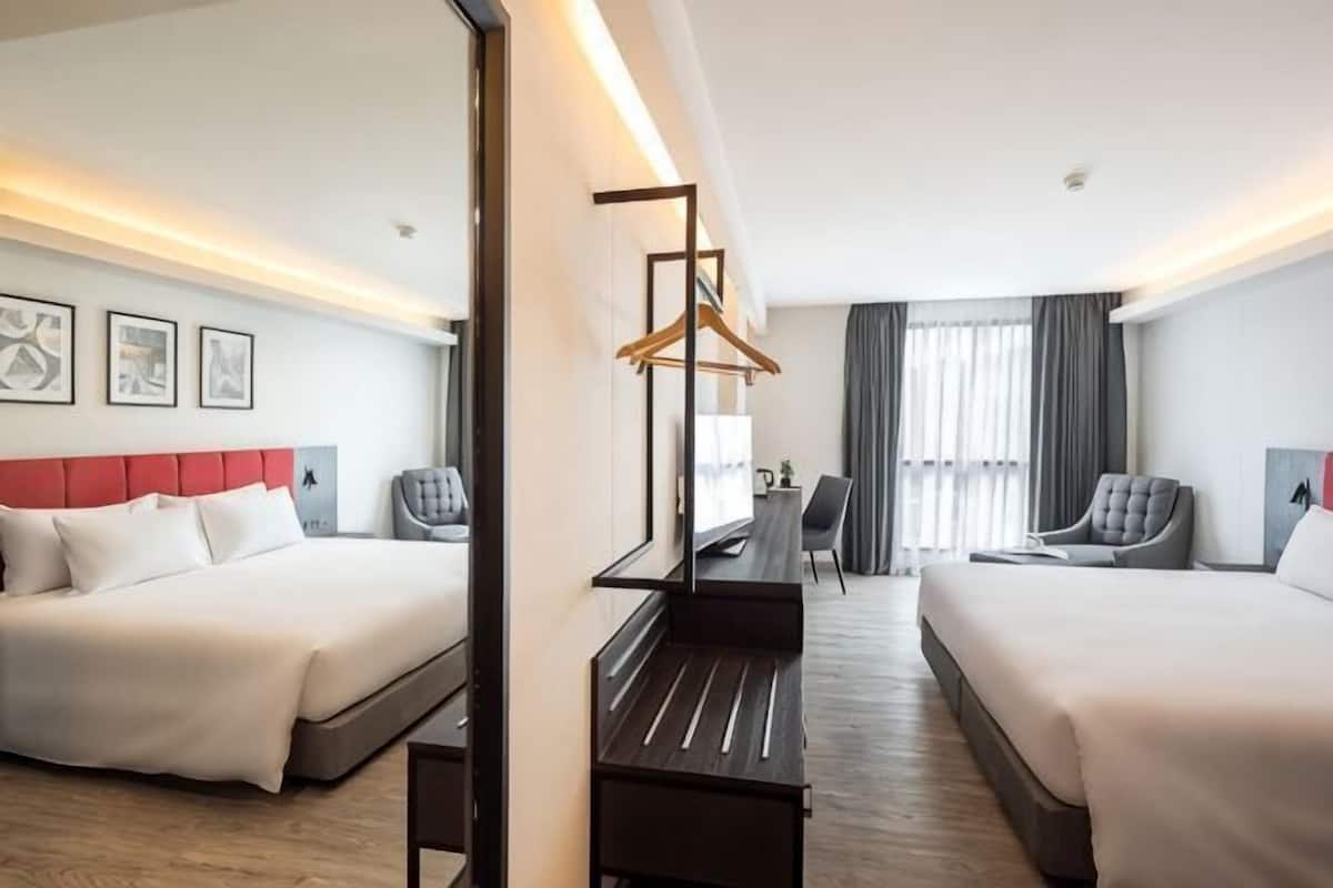 A hotel room with two beds, a desk, a chair, and a mirror.