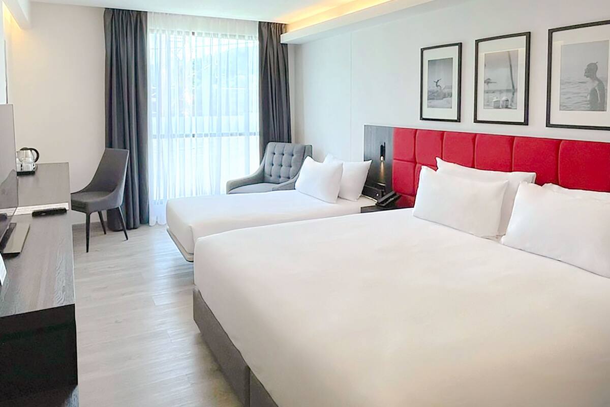 A hotel room with two beds, a desk, a chair, a TV, and a window with curtains.