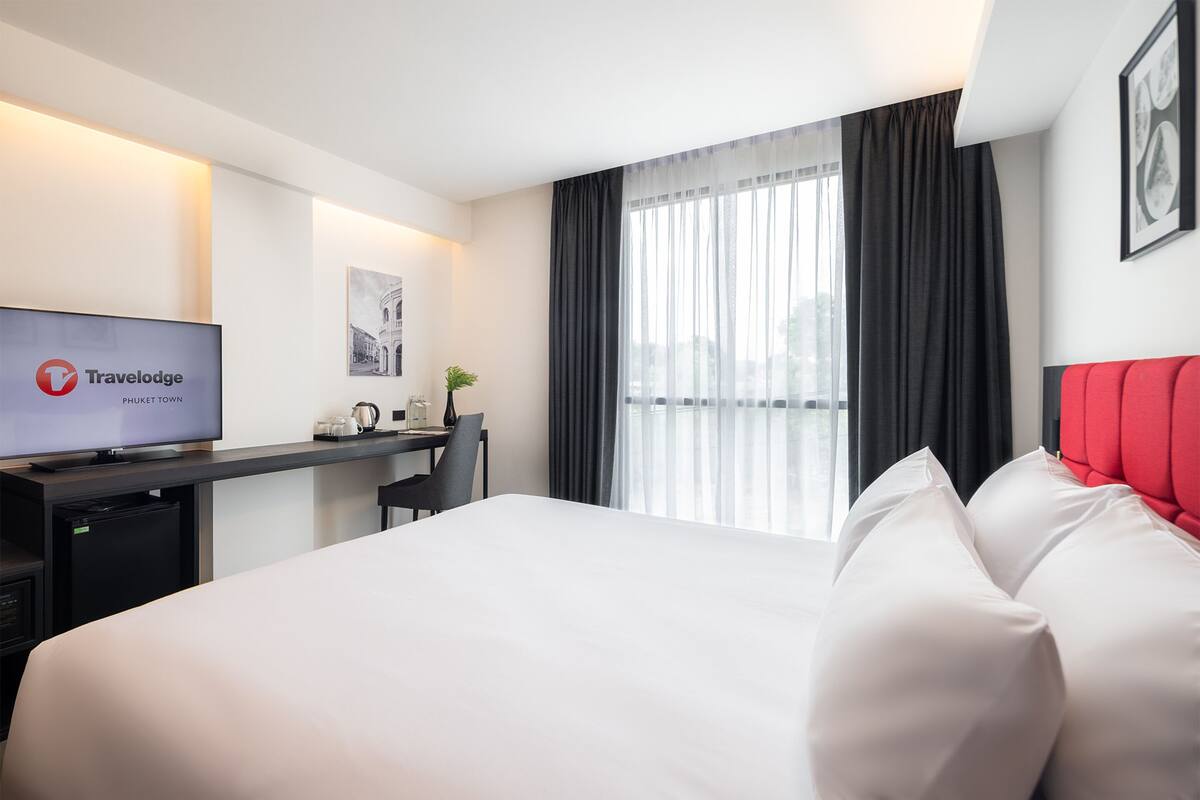 A hotel room with a bed, a desk with a TV, a chair, and a window with curtains.