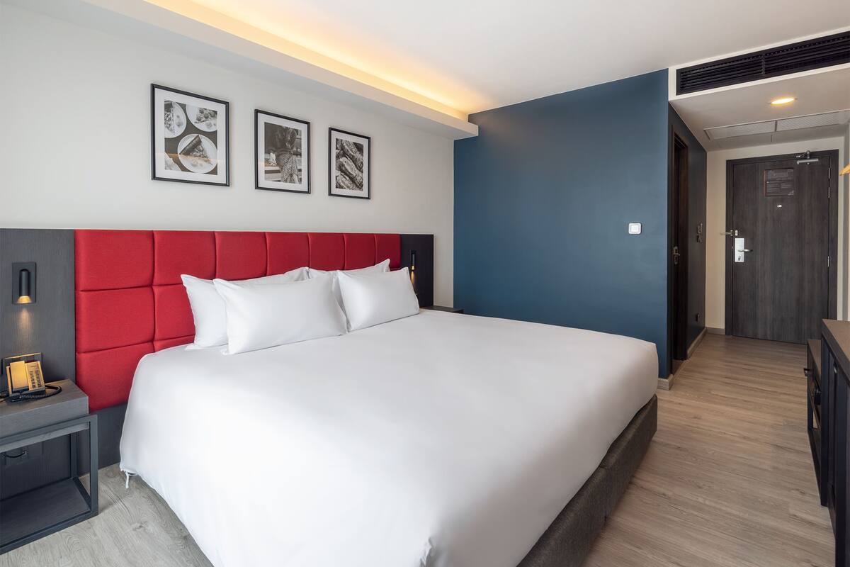 A modern hotel room with a large bed, a red headboard, and framed artwork on the wall.