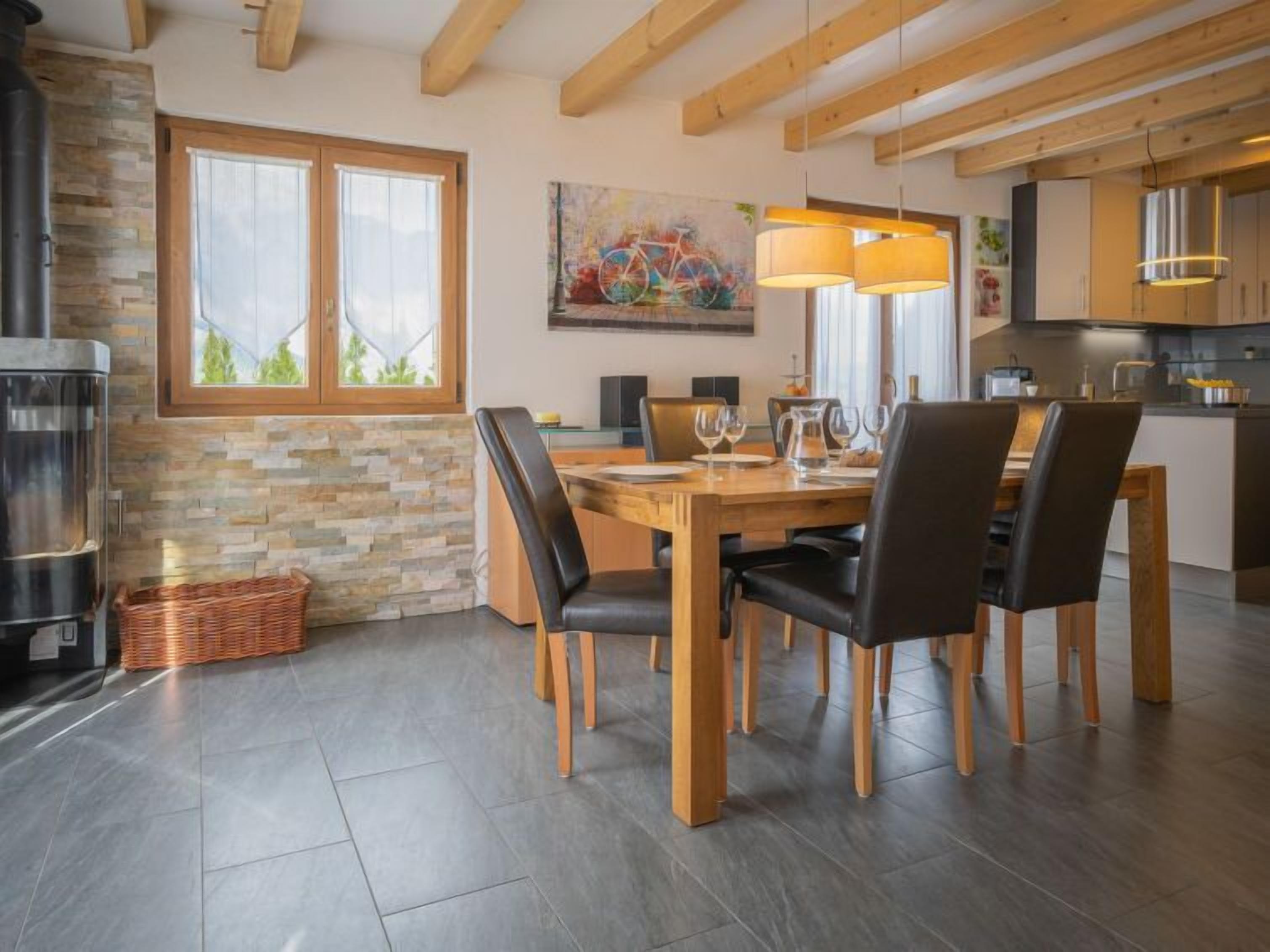 Un espace repas moderne avec une table et des chaises en bois, un mur en pierre et une grande fenêtre.